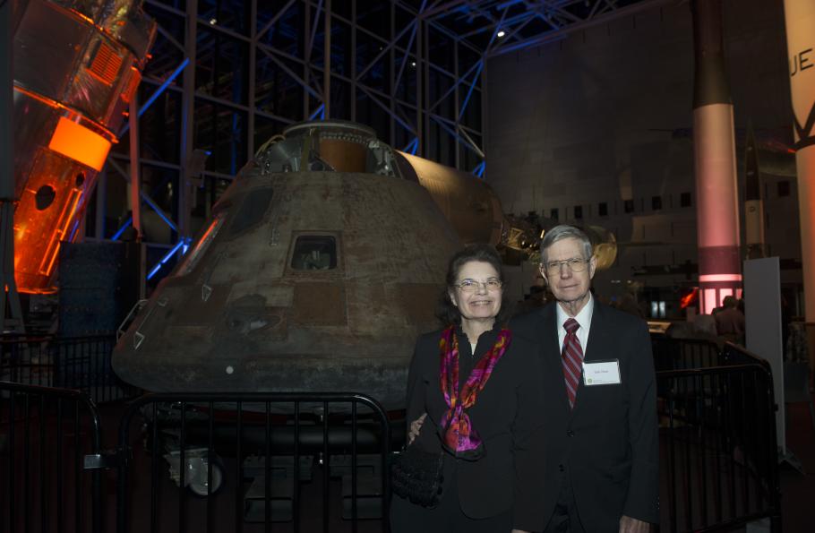 A couple consisting of a white female (left) and male (right) post in front of the conic-shaped metal Apollo Command Capsule.